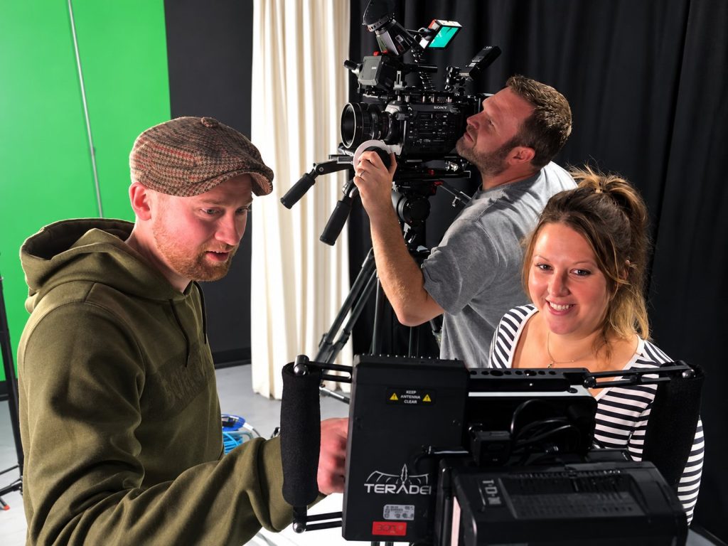 Three crew members working around a camera in a studio