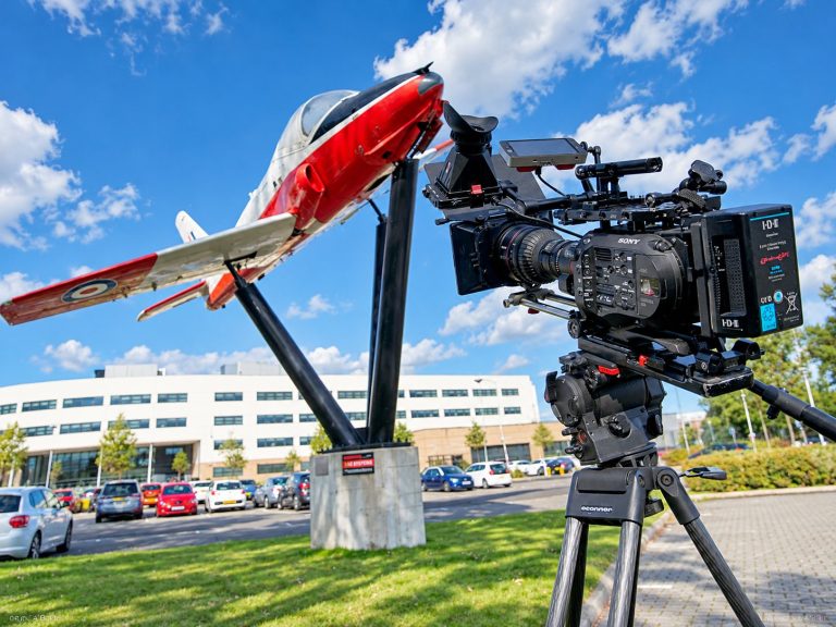 A camera set up in front of a jet aircraft on display outside a building